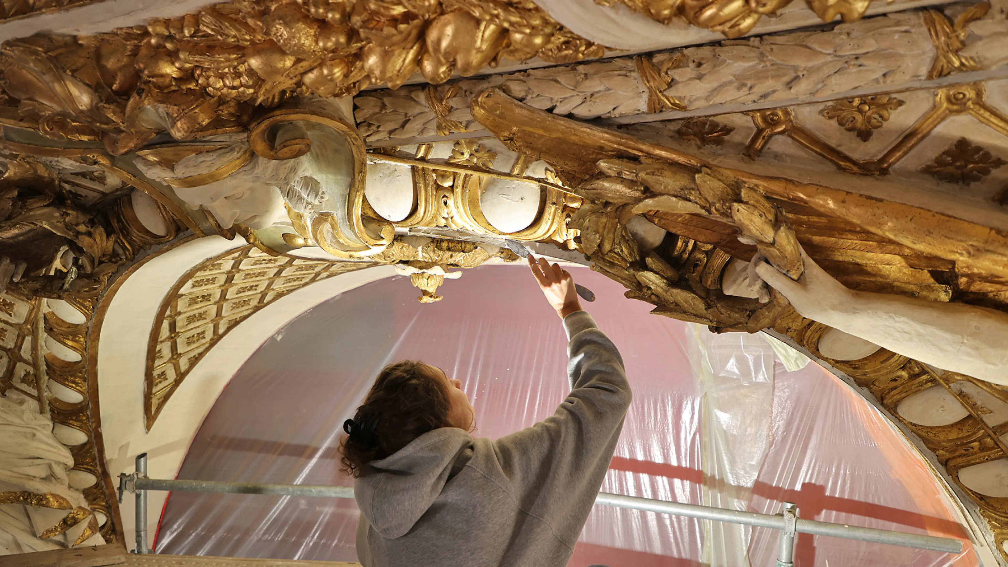 Un artisan restaure avec minutie un décor architectural doré de la voûte de l'Opéra.