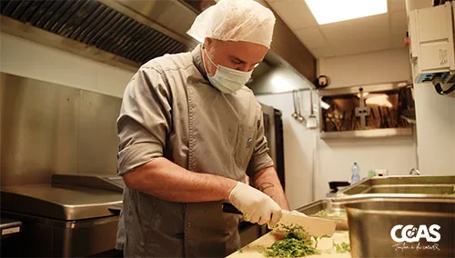 Agent de l’UPC découpant des herbes fraîches sur un plan de travail en cuisine.