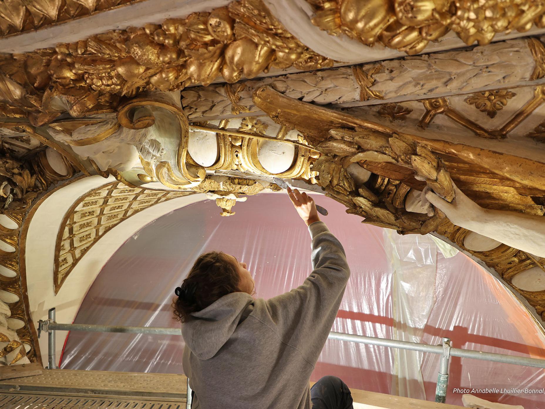 Un artisan restaure avec minutie un décor architectural doré de la voûte de l'Opéra.