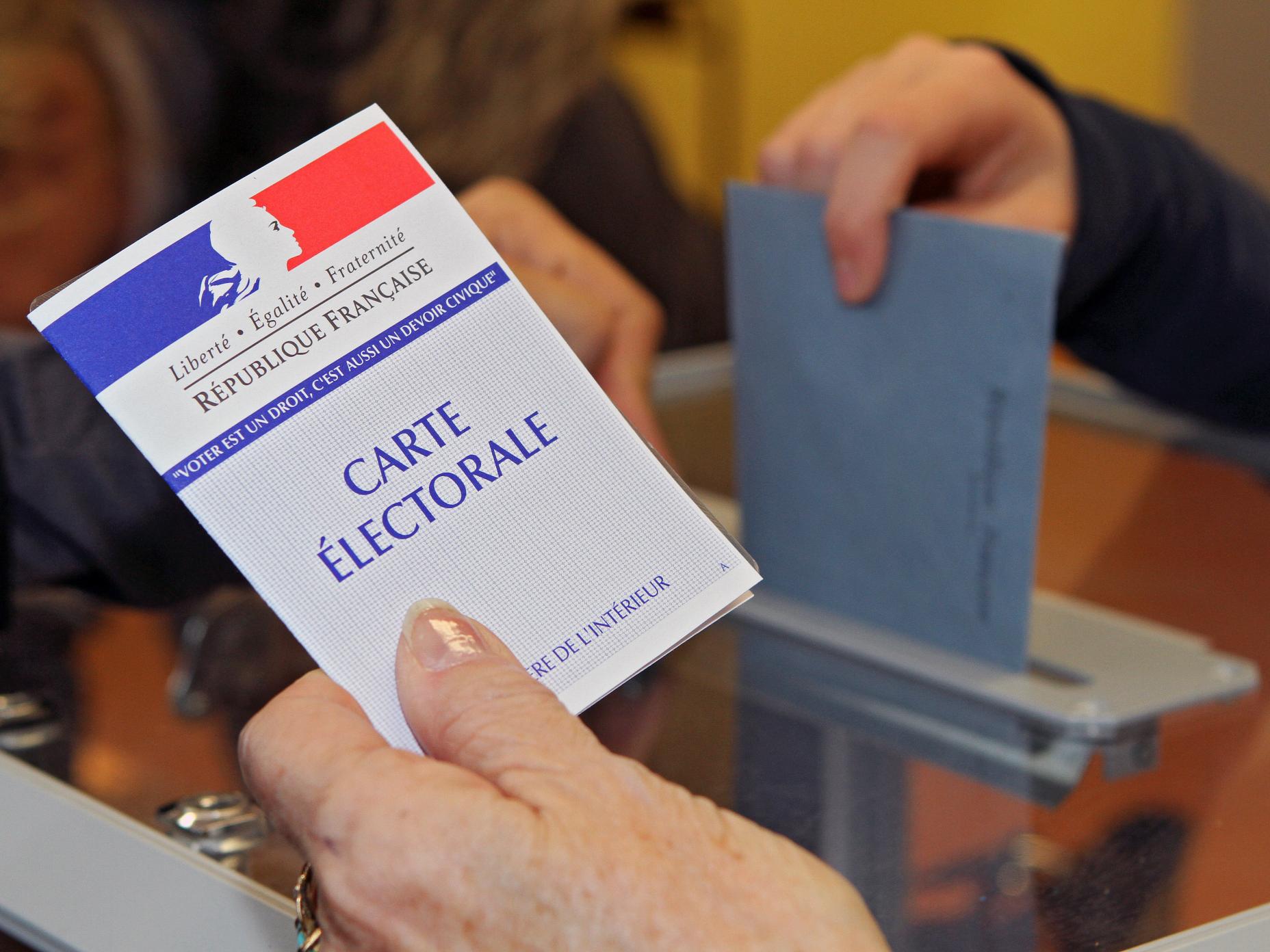 La photo montre la main d'un électeur présentant sa carte électorale