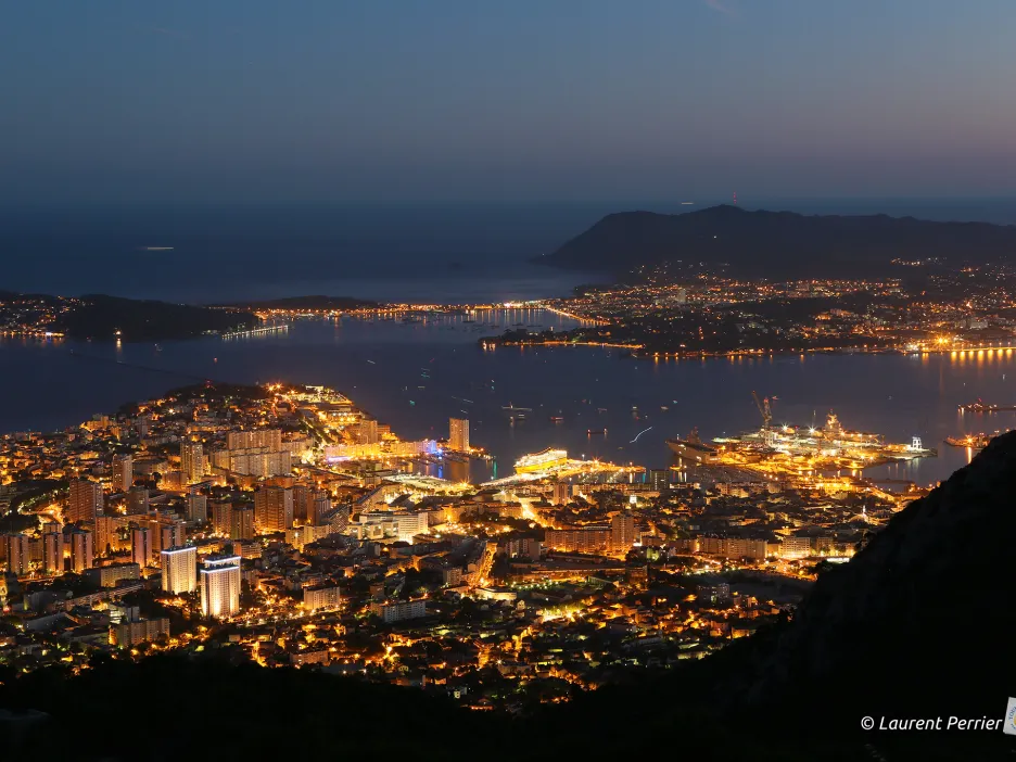 Photographie de nuit prise depuis les Monts Toulonnais. On peut y deviner l'Arsenal et la Rade de Toulon, ainsi que toute la ville et ses éclairages