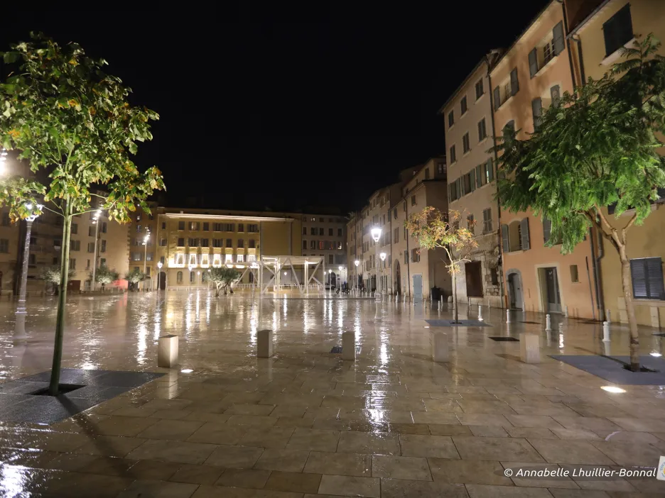 Photographie de nuit montrant une partie de la place de l'Equerre à Toulon. Le sol légèrement mouillé permet de refléter les éclairages des lanternes disposés sur la place.