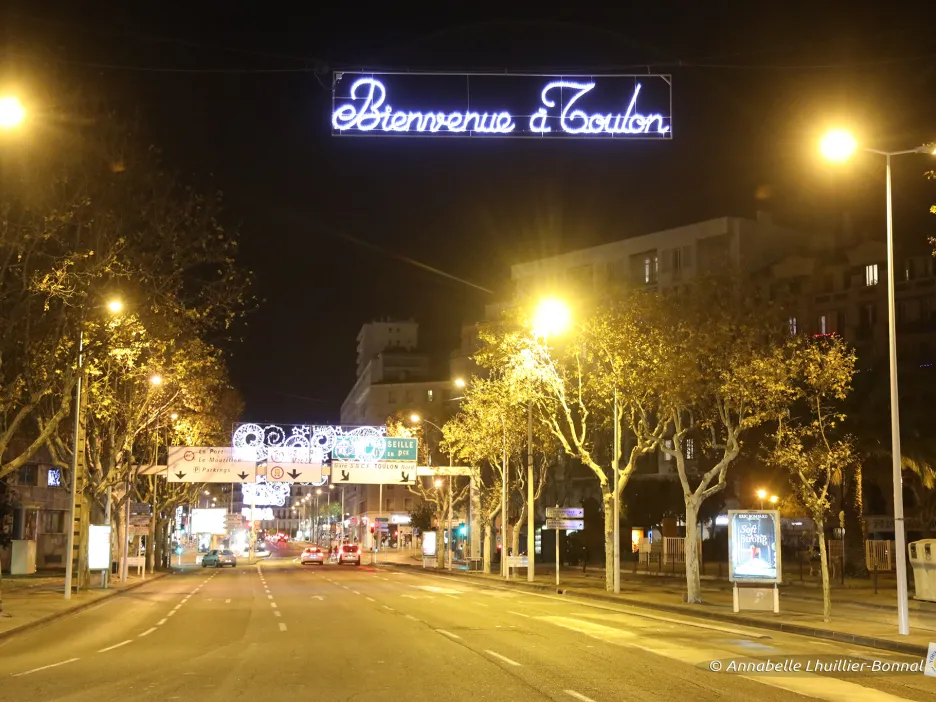 Photographie de nuit du boulevard de Strasbourg. Des éclairages de célébration y ont été installés comme le "Bienvenue à Toulon" au dessus de la route, ou des symboles éclairés que l'on peut voir plus loin 
