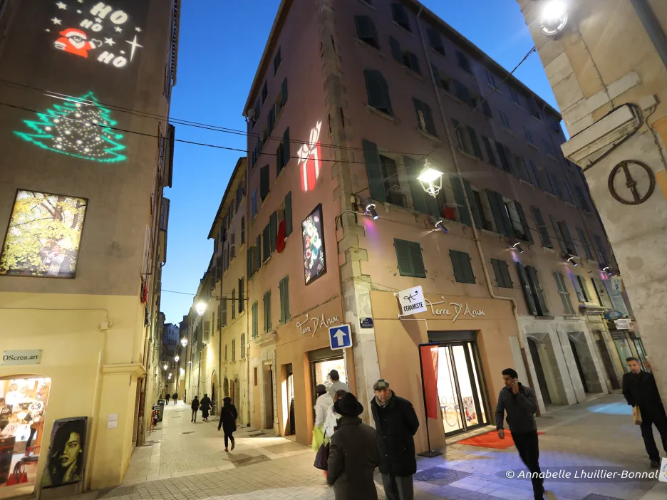 Photographie de nuit de la Rue des Arts décorée pour les fêtes de fin d'année : on peut voir sur le mur du bâtiment à gauche de la photo un sapin ainsi qu'un père Noël colorés projetés sur la façade 