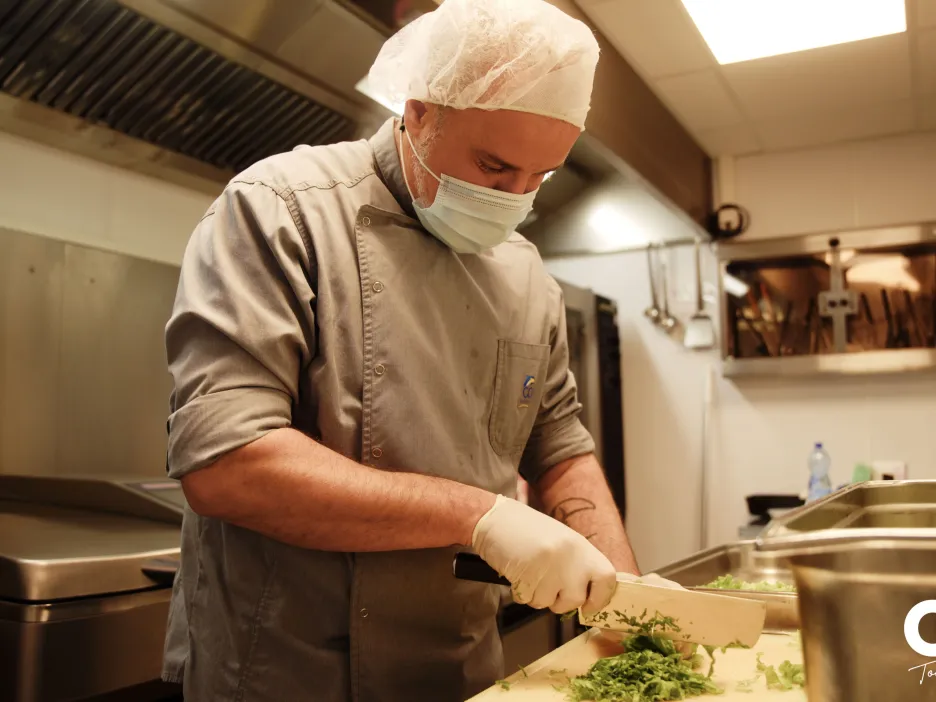 Agent de l’UPC découpant des herbes fraîches sur un plan de travail en cuisine.